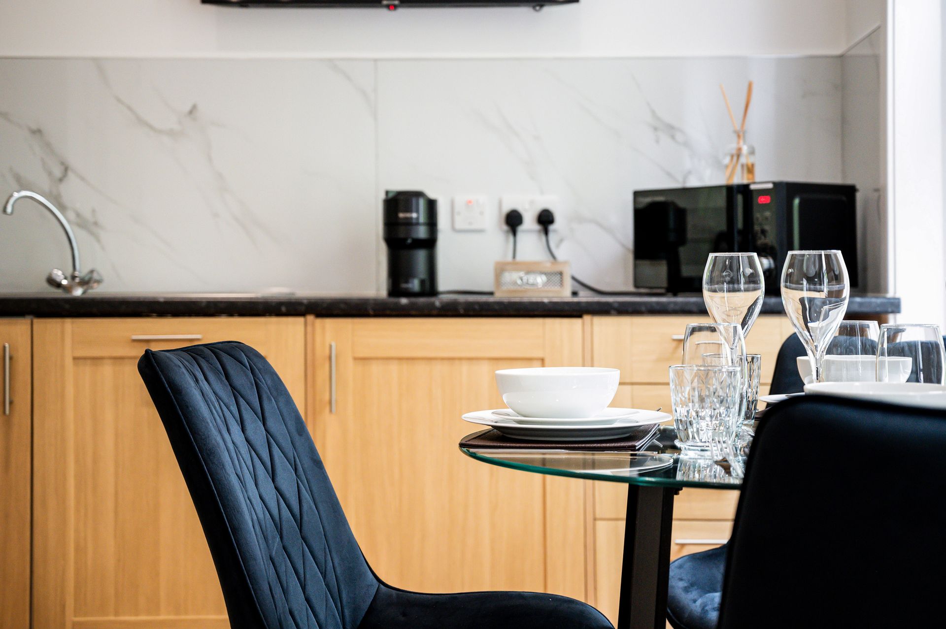 Modern kitchen with wood cabinets, black countertop, dining table, and wine glasses near a coffee maker