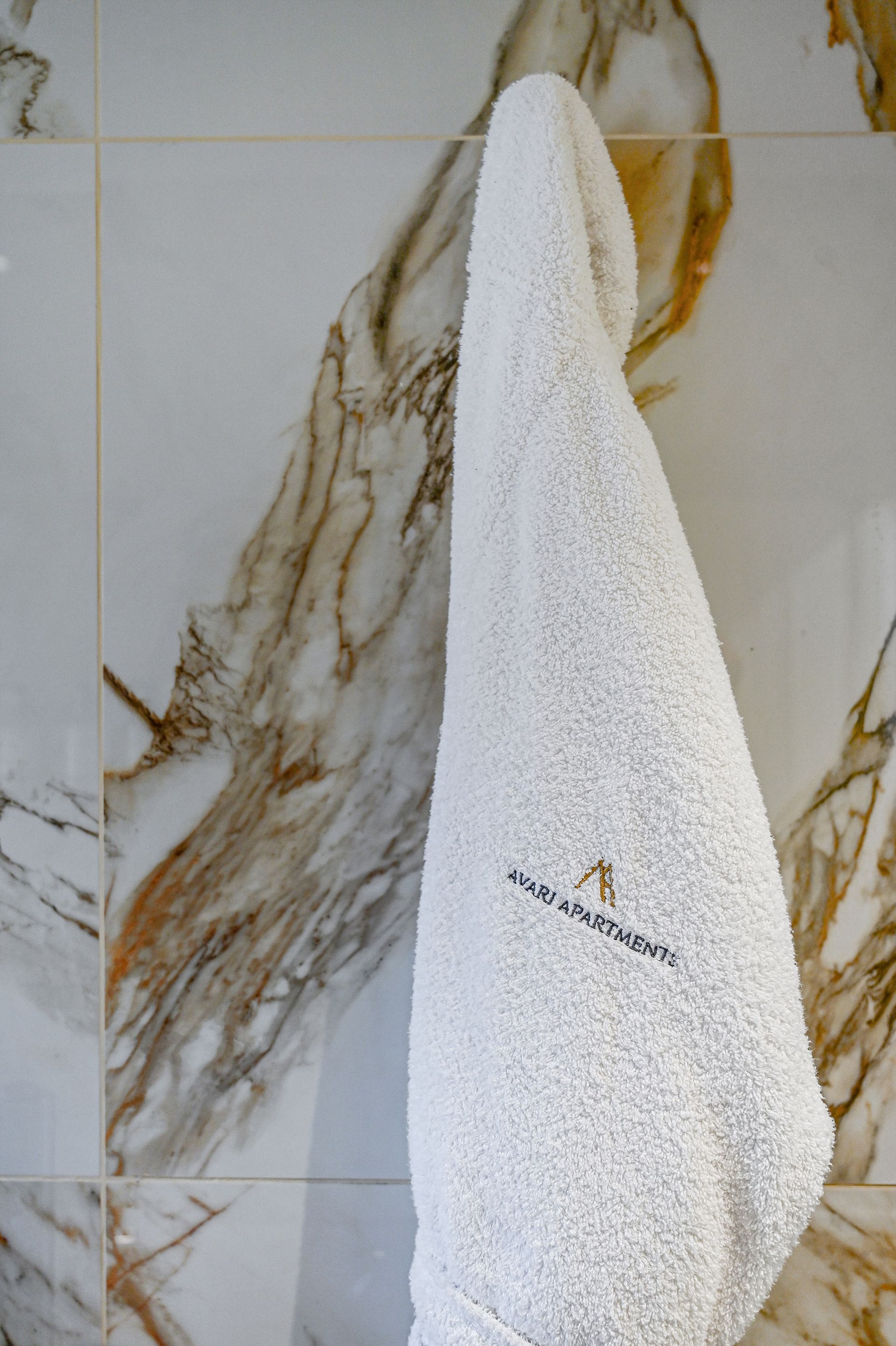 White towel hanging on a hook against a marble-tile wall