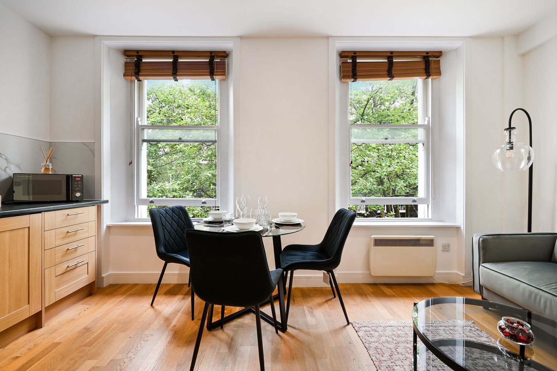 Bright dining area with round table, black chairs, wooden floors, and large windows
