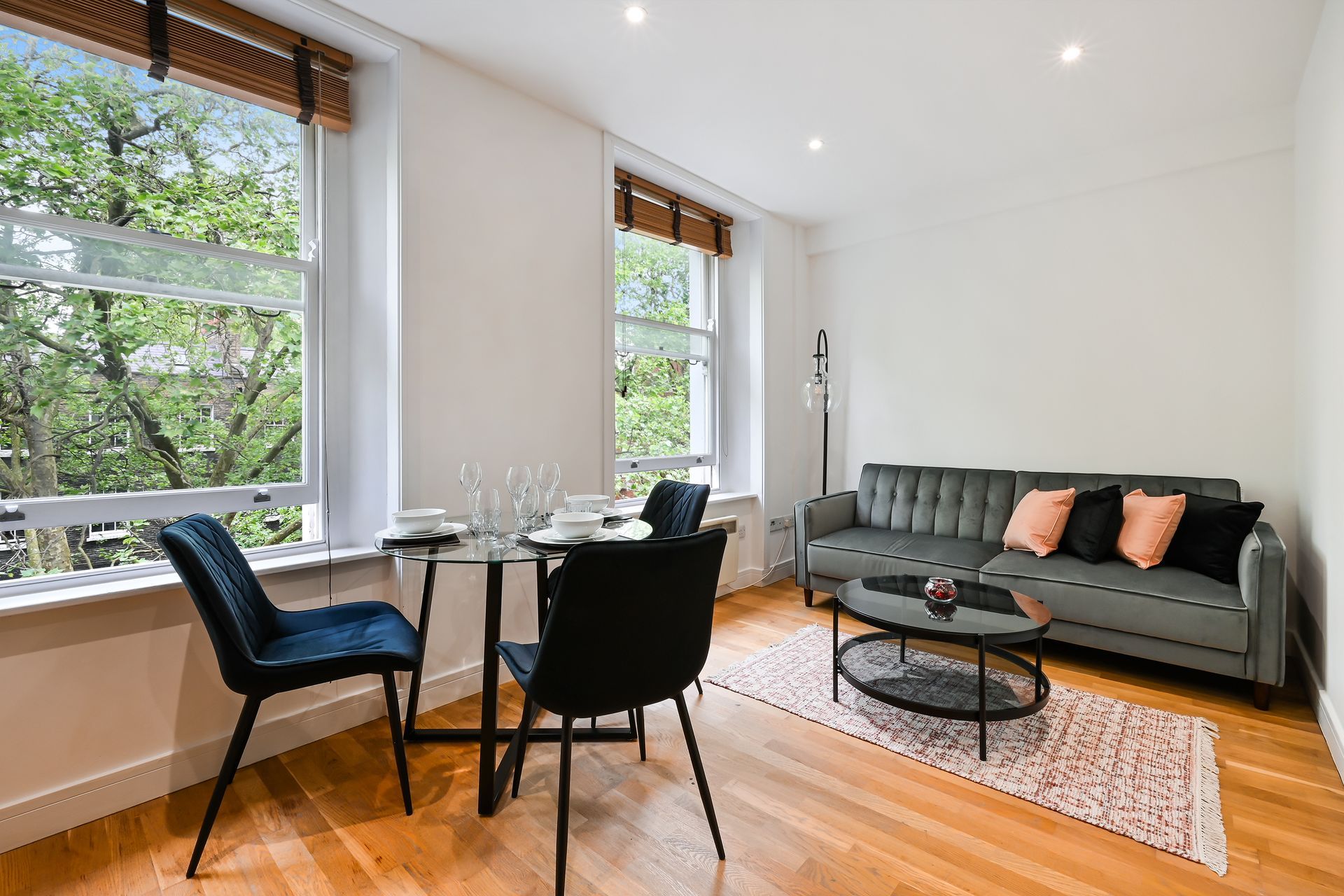 Bright living room with large windows, dining table, gray sofa, and wooden floors