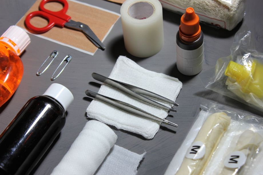 Medical first-aid supplies and tools arranged on a gray surface, including scissors, tweezers, bandages, and bottles