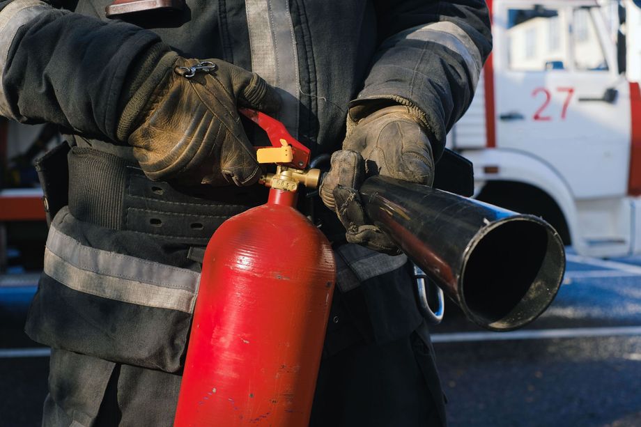 Firefighter holding a red extinguisher and black hose nozzle in front of an emergency vehicle