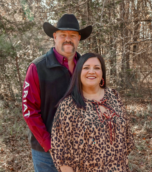 Smiling couple in cowboy attire posing with two dogs at a Louisiana-themed booth with C&W branding