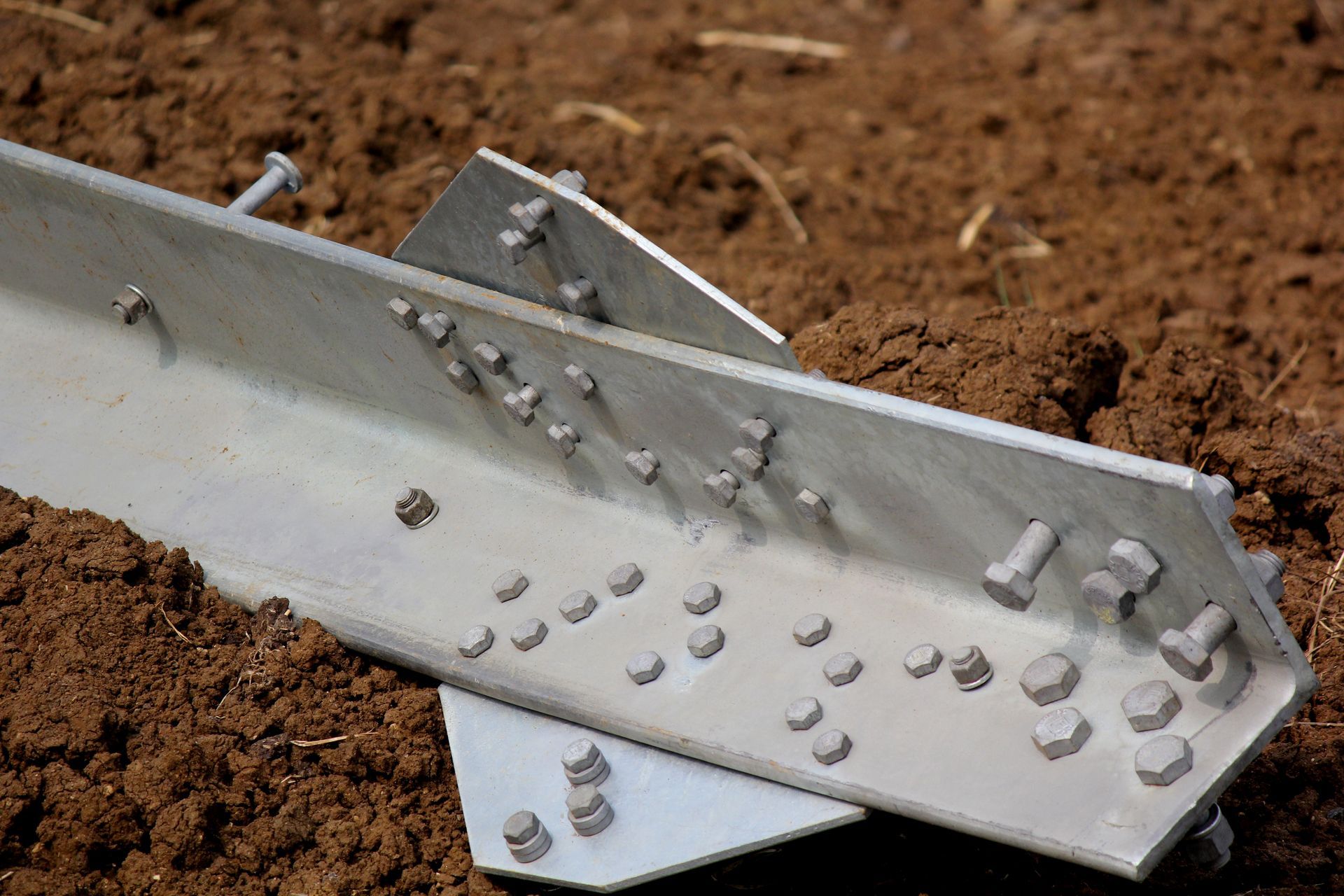 Galvanized steel beam with bolts and plates resting on soil at a construction site.
