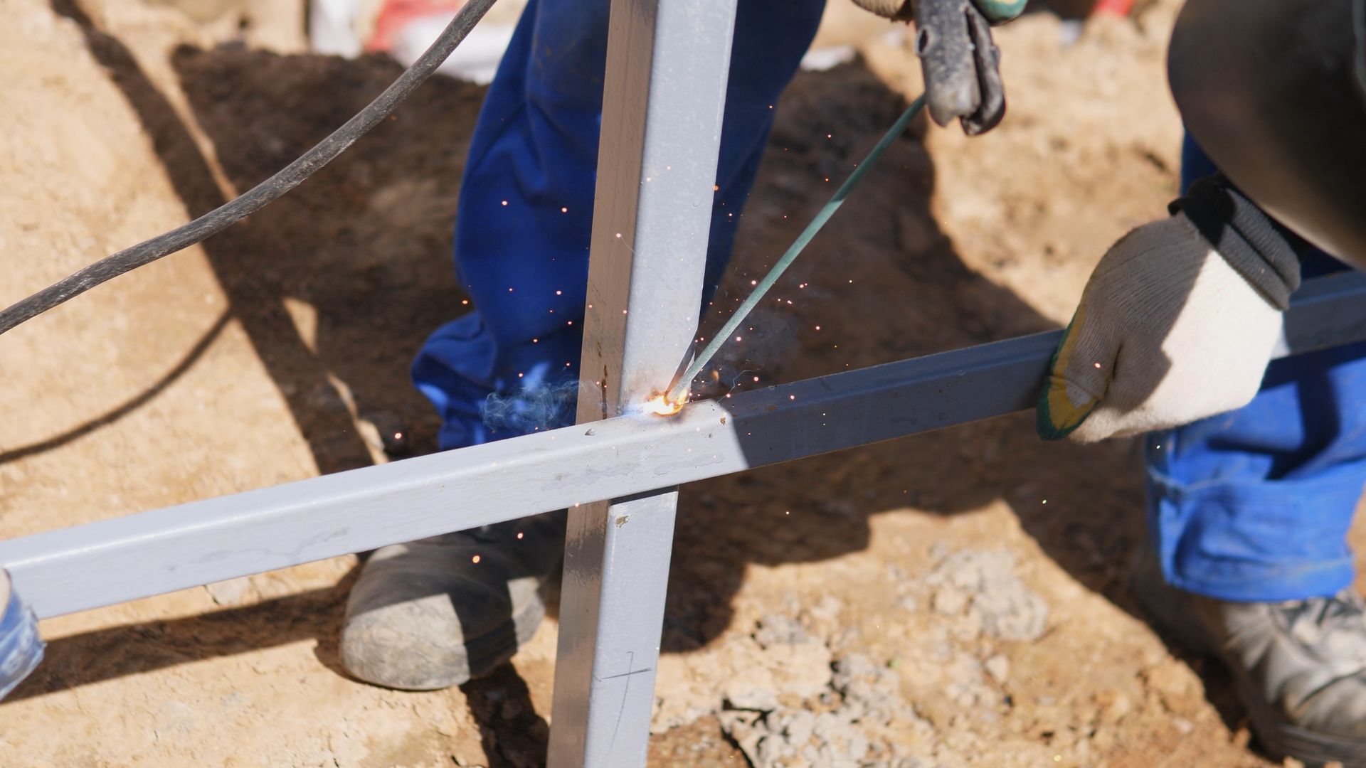 Worker cutting a metal beam with an angle grinder at a construction site.