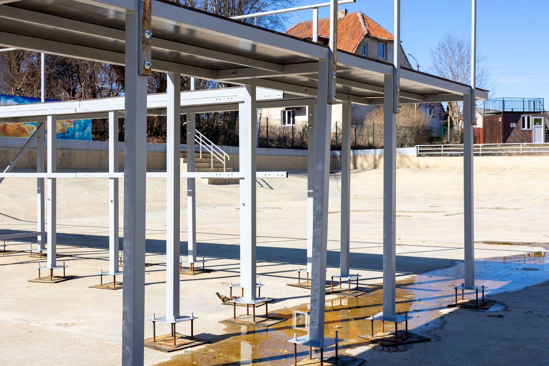 Steel canopy frame with anchor bolts on concrete outdoor stadium platform.
