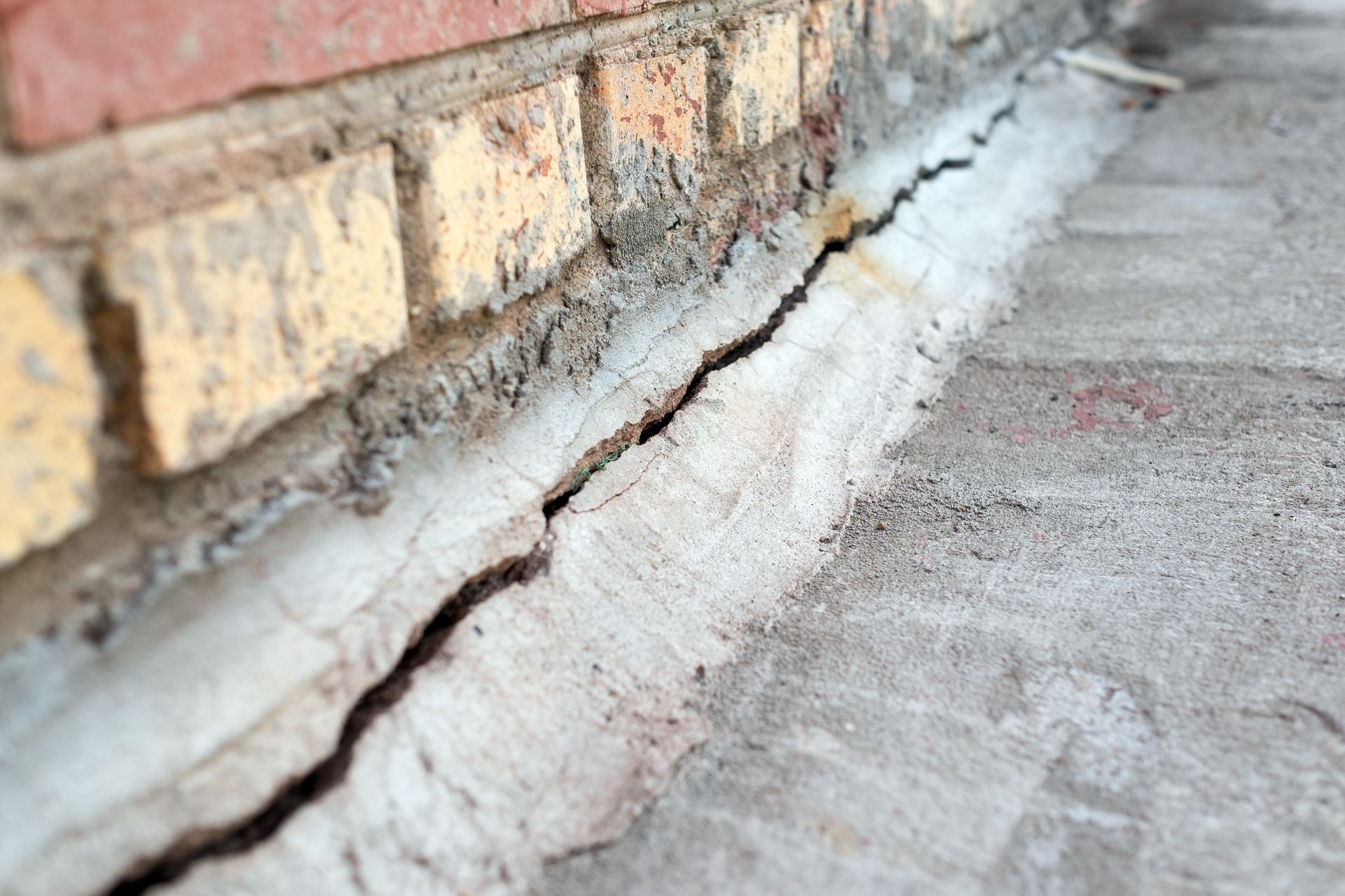 Crack along a building foundation where concrete meets a brick exterior wall.