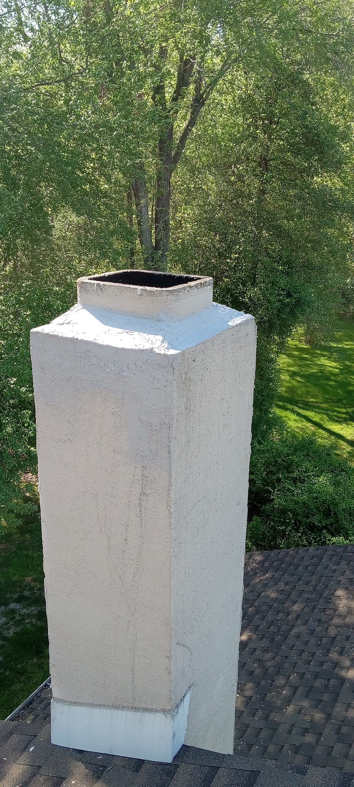 White outdoor pedestal or chimney with a black top in a grassy yard with trees behind it