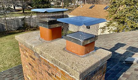 Two metal chimney vents with blue caps on a brick rooftop in sunlight
