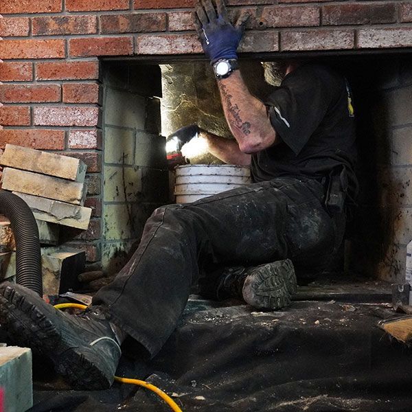 Person working inside a brick fireplace, cleaning or repairing the hearth.