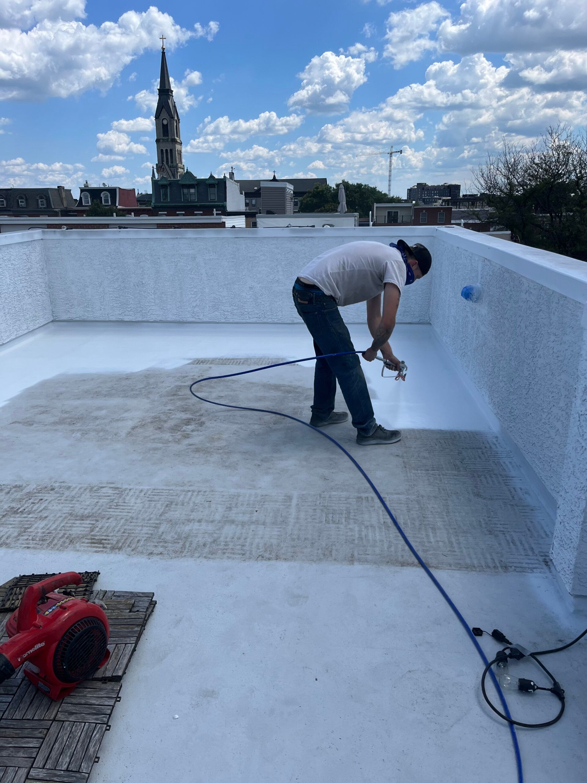 Worker spraying waterproof coating inside a rooftop pool or terrace under a cloudy sky