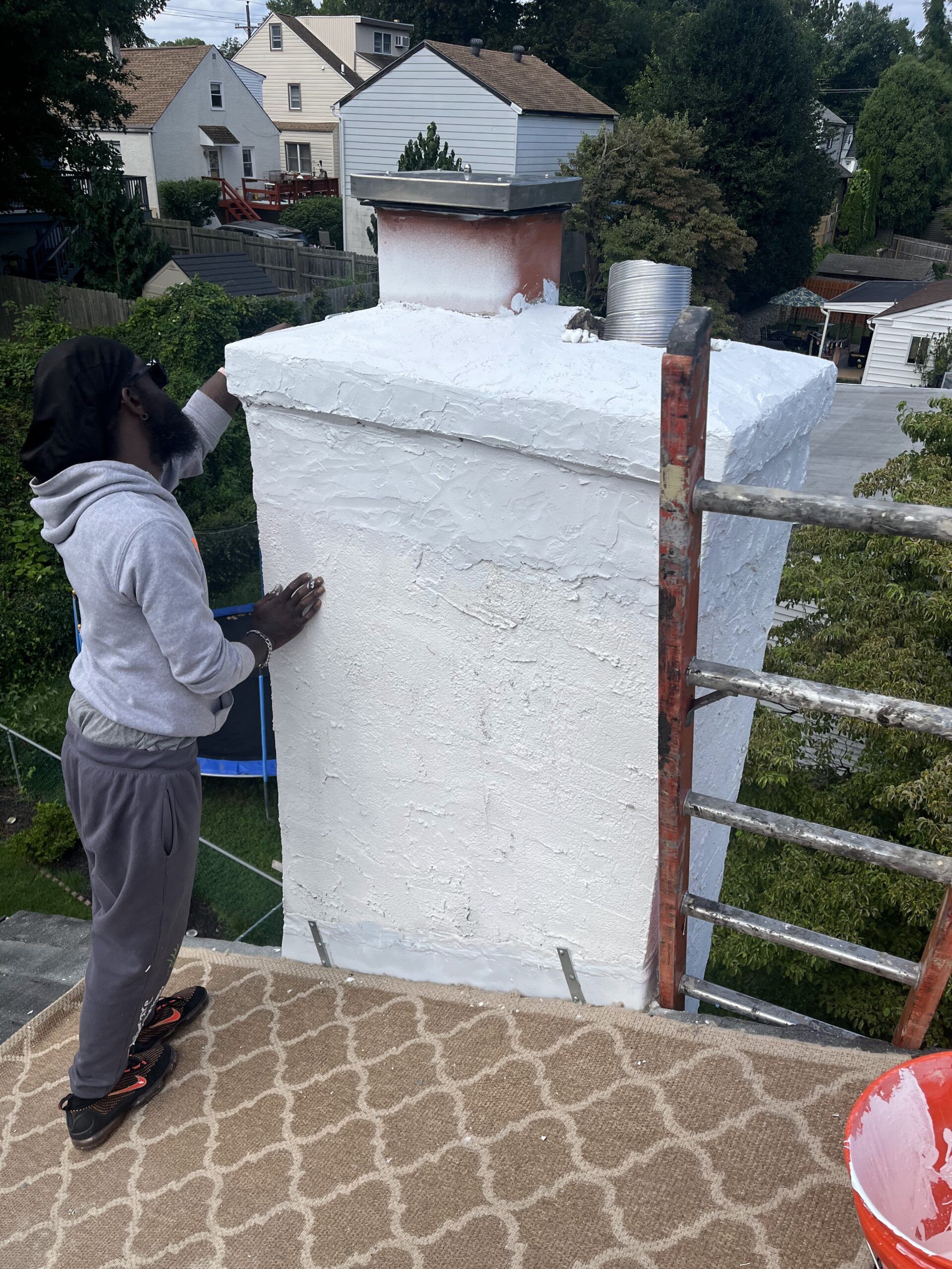Person painting a large white wall on a rooftop terrace with houses in the background