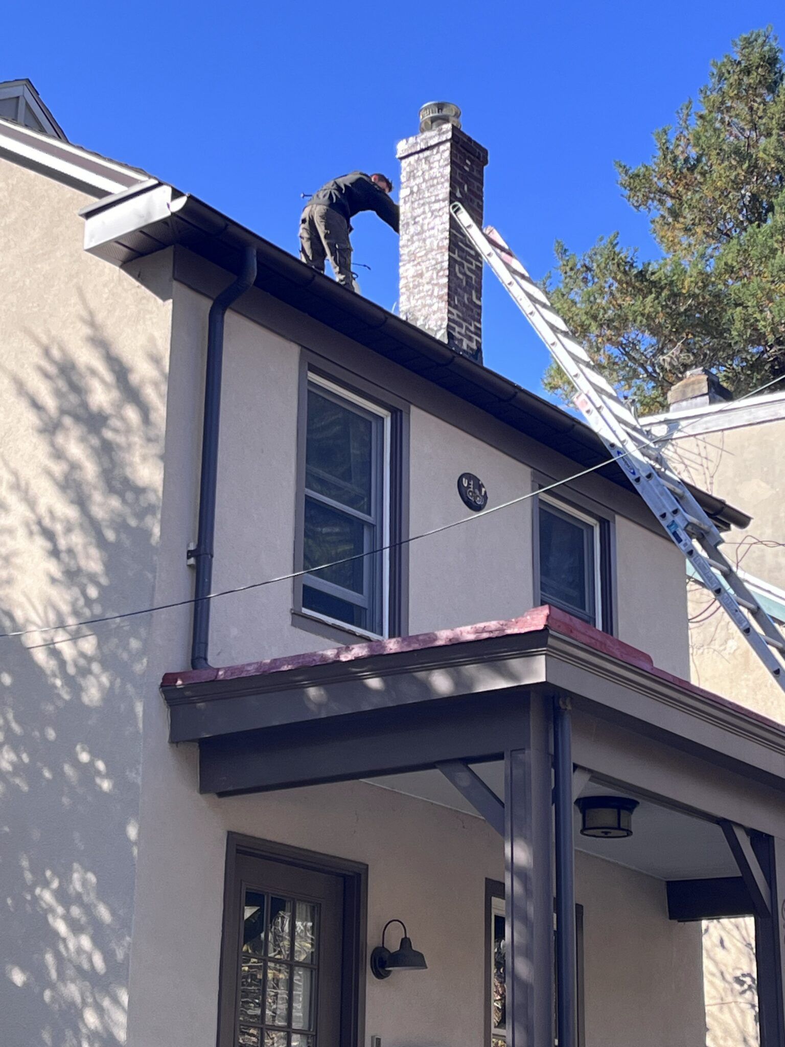 Two-story stucco house with dark trim, balcony, and chimney, viewed from below under a blue sky