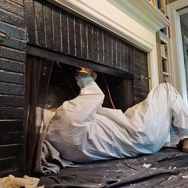 Worker in a white protective suit cleaning a fireplace inside a home