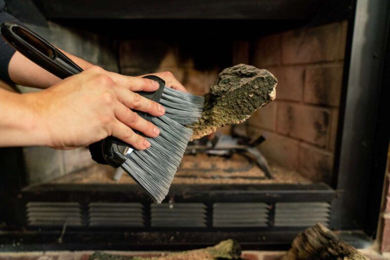 Hand brushing ashes from fireplace grate with a dustpan and brush