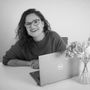 A woman is sitting at a desk with a laptop and a vase of flowers.
