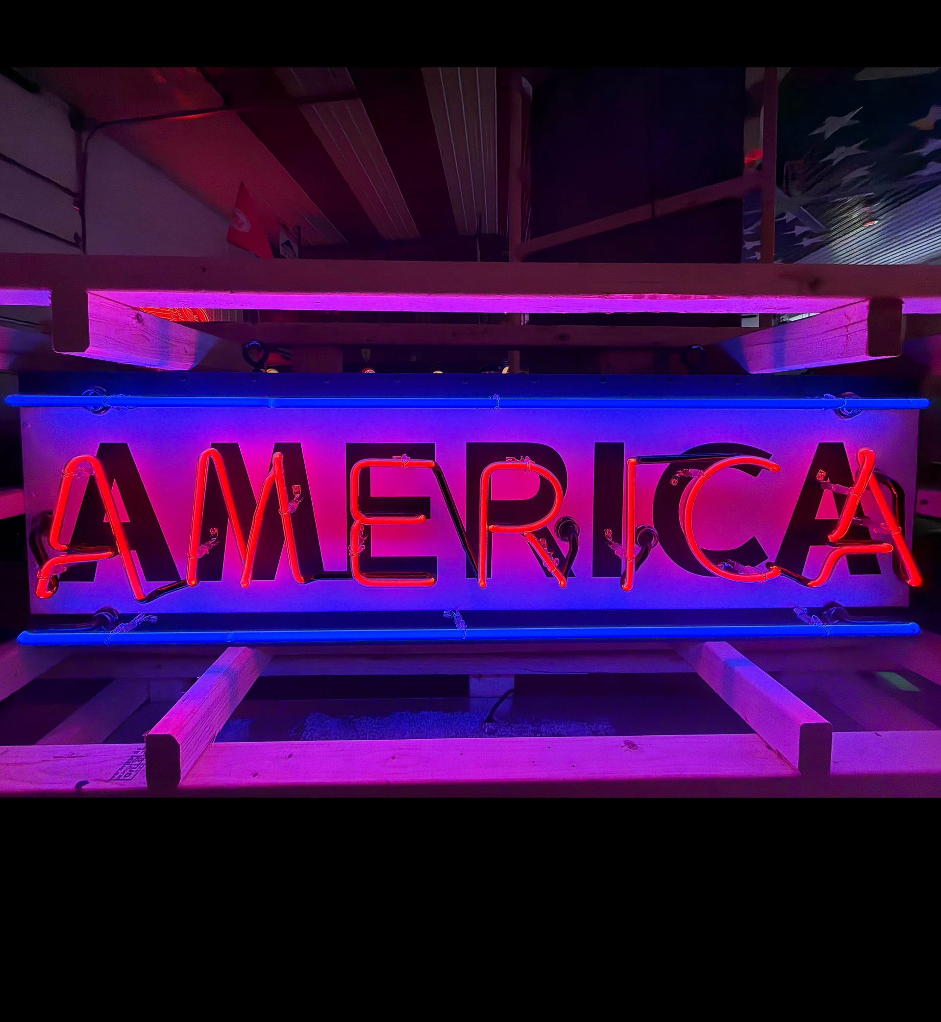 Neon-lit sign reading “AMERICA” in red and blue, glowing against a dark background.
