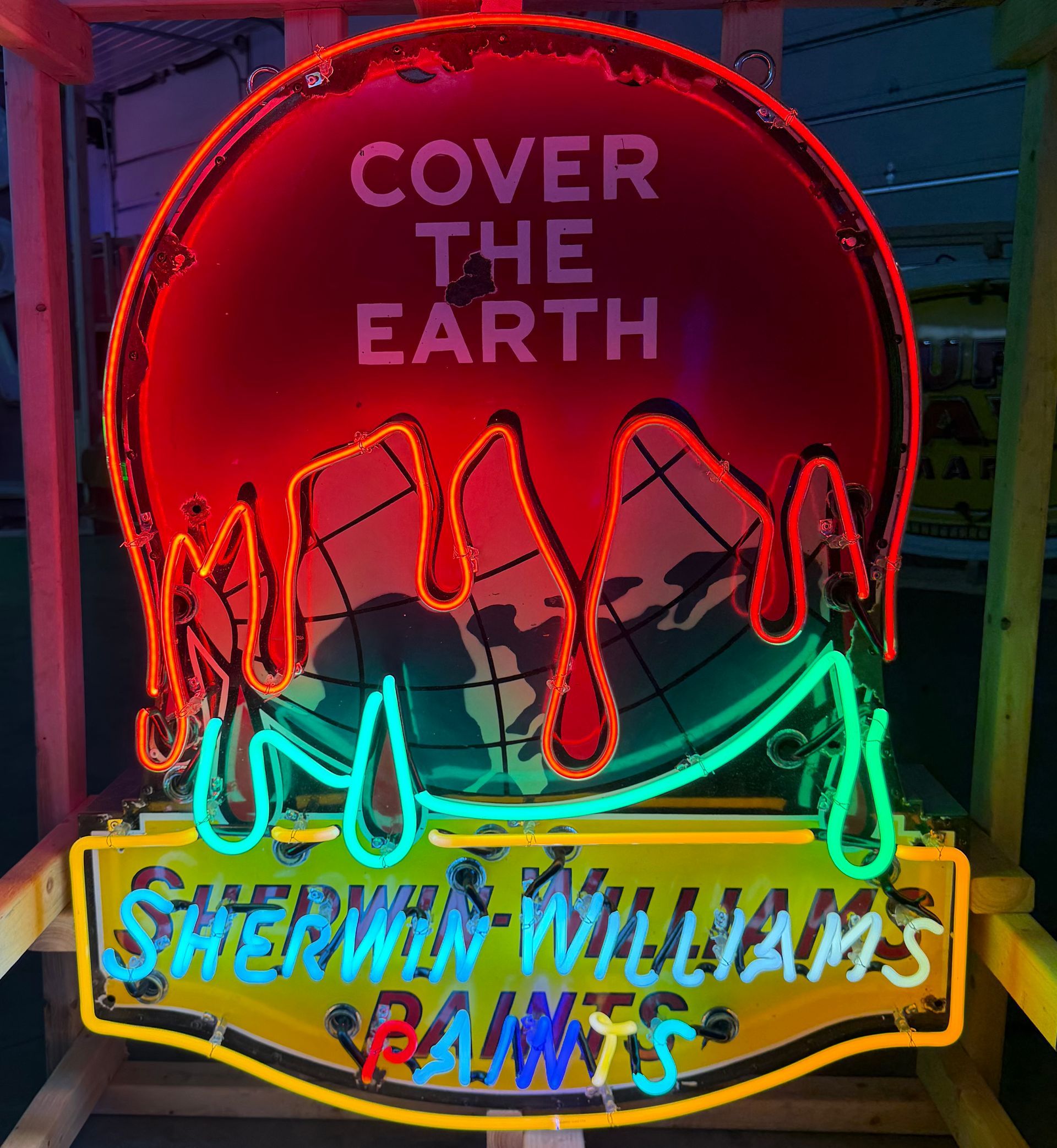 Neon Sherwin-Williams sign with red paint dripping over a globe, and the words “Cover the Earth”