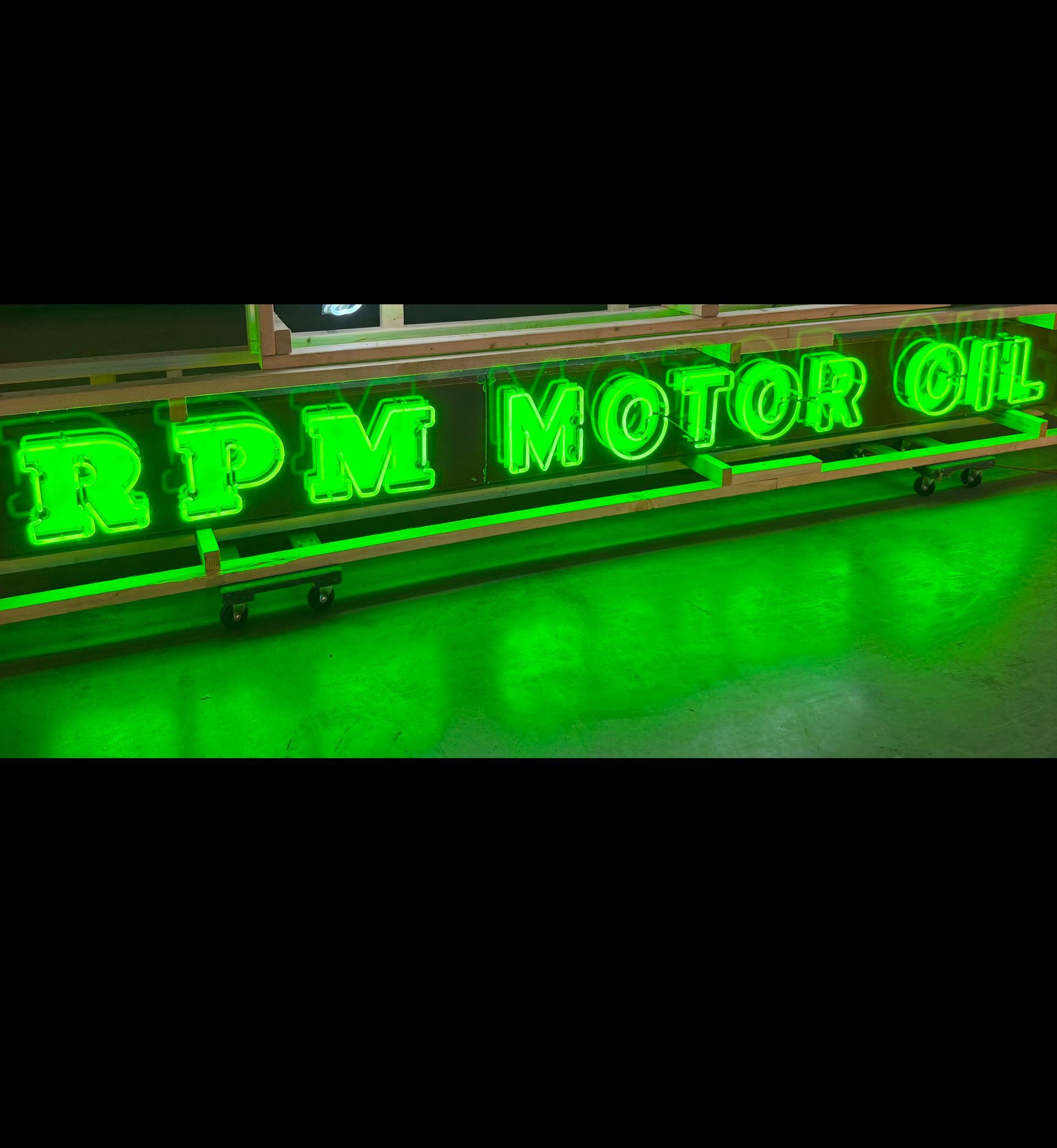 Neon green “RPM MOTOR OIL” sign glowing on a floor, with bright reflected light.