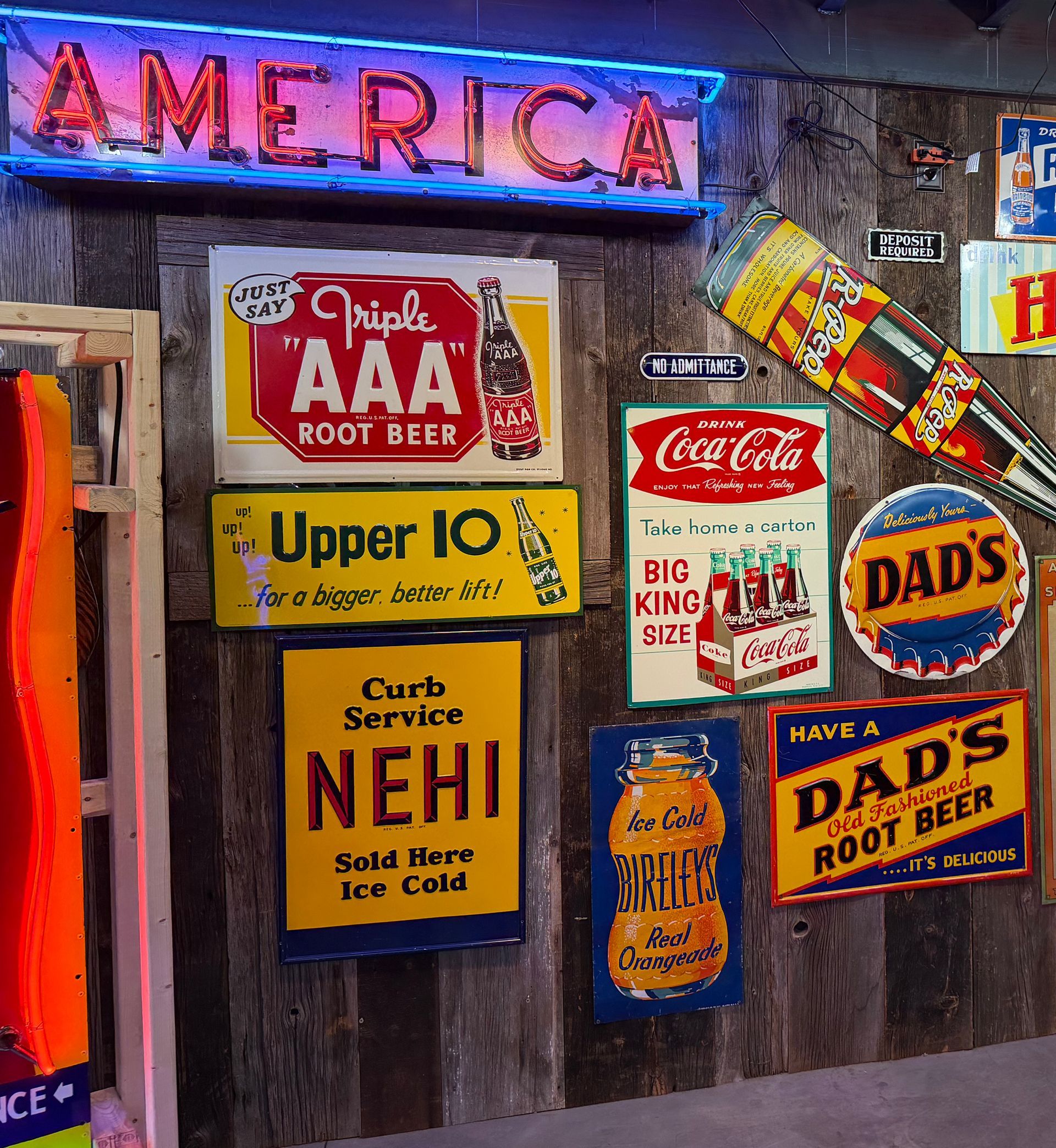 Wall of colorful old advertising soda and beer signs, including neon “AMERICA” and “DAD’S Root Beer.”
