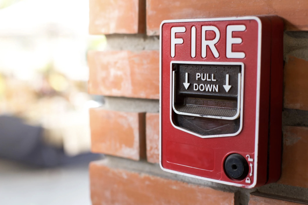 A red fire alarm is mounted on a brick wall.