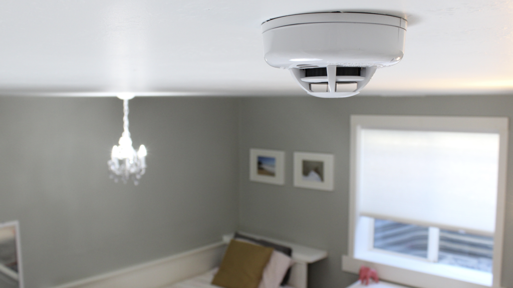 A bedroom with a smoke detector on the ceiling.