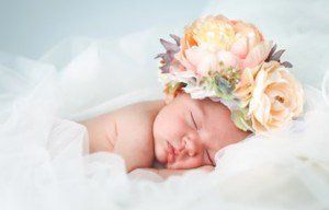 A newborn baby is sleeping with a flower crown on her head.
