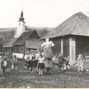 A group of children are standing in front of a wooden building in a black and white photo.