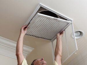 A man is cleaning an air vent on the ceiling.