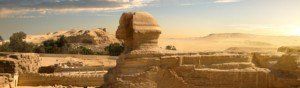 A statue of a sphinx in the desert with mountains in the background.