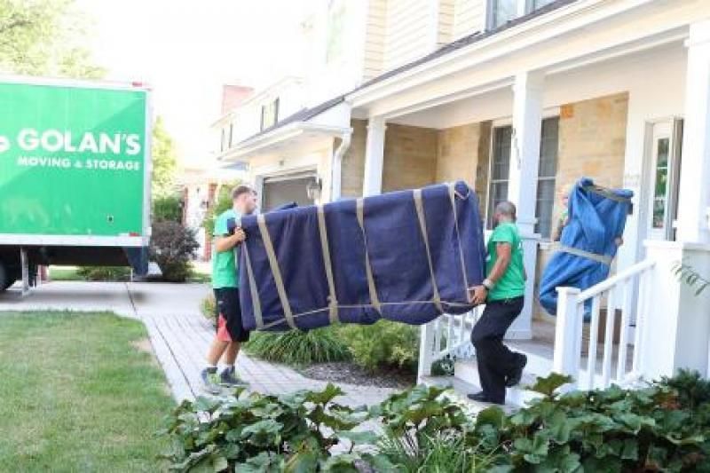 A couple of men are carrying a large piece of furniture in front of a house.