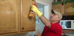 A man wearing yellow gloves is cleaning a cabinet in a kitchen.