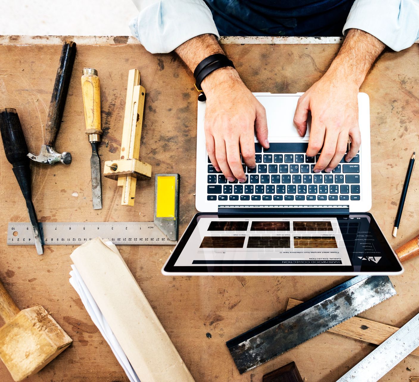 A person using a laptop amidst carpentry tools, possibly researching wood stain options.