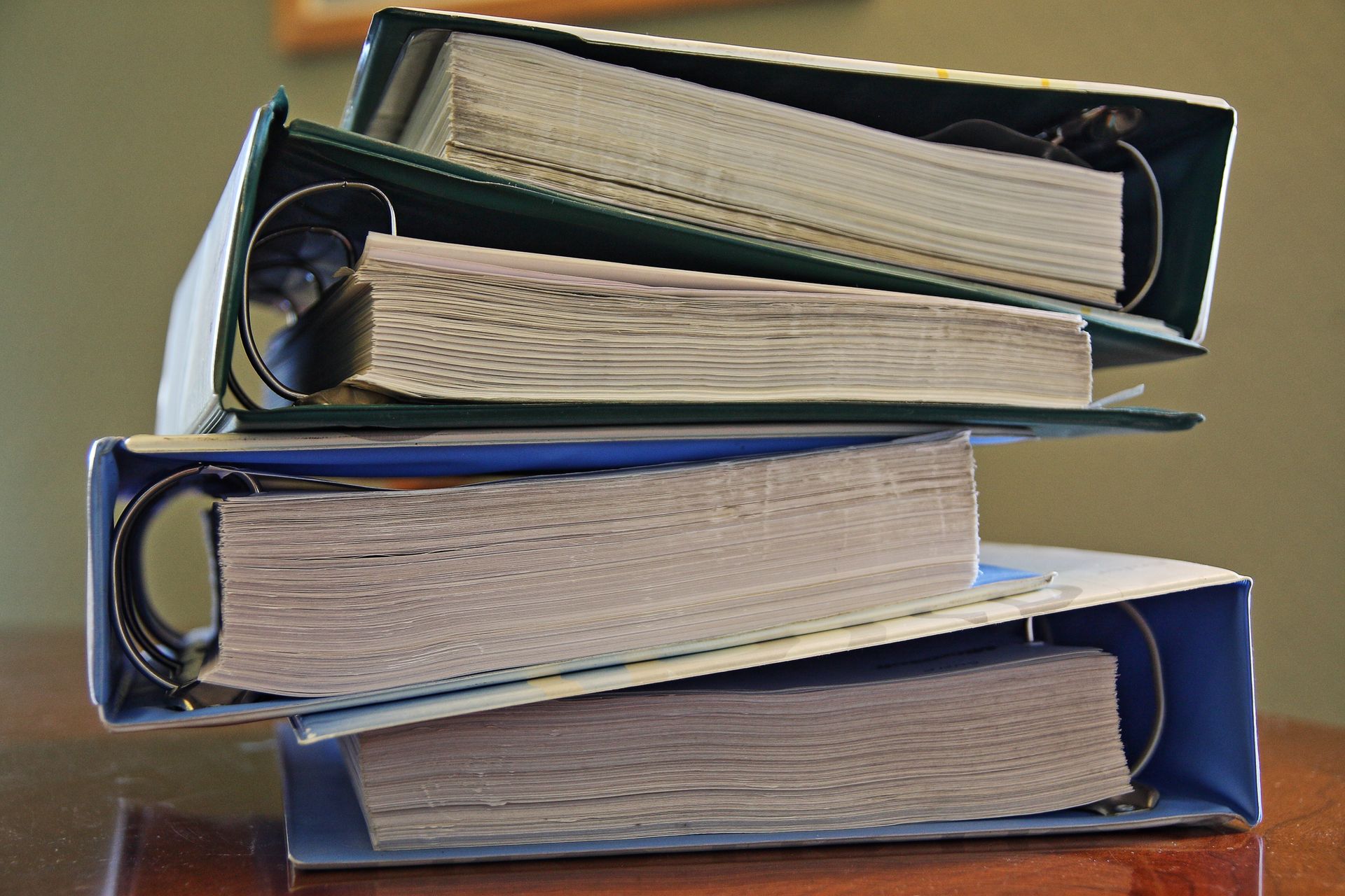 Three binders stacked on top of each other, filled with paper. The binders are open, and are blue and green.