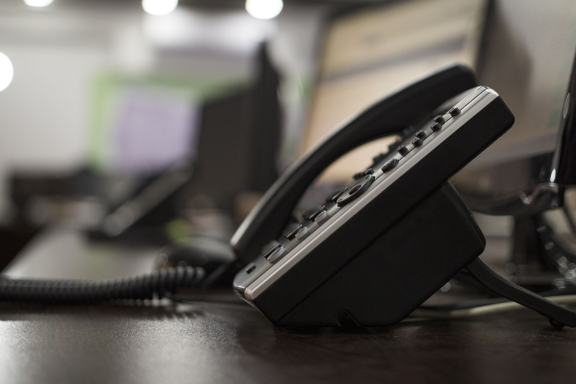 Black office phone on a desk, close-up; blurred background of office space.
