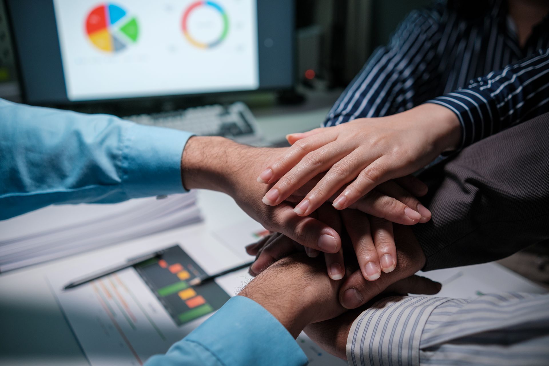 Hands piled together in a team huddle, in front of a computer screen with a pie chart.