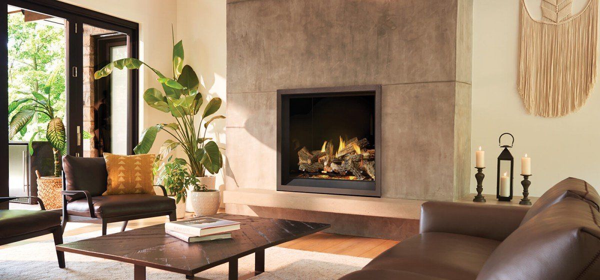 Un salon avec une grande cheminée en pierre grise, un canapé en cuir marron, une table basse et une plante verte feuillue.