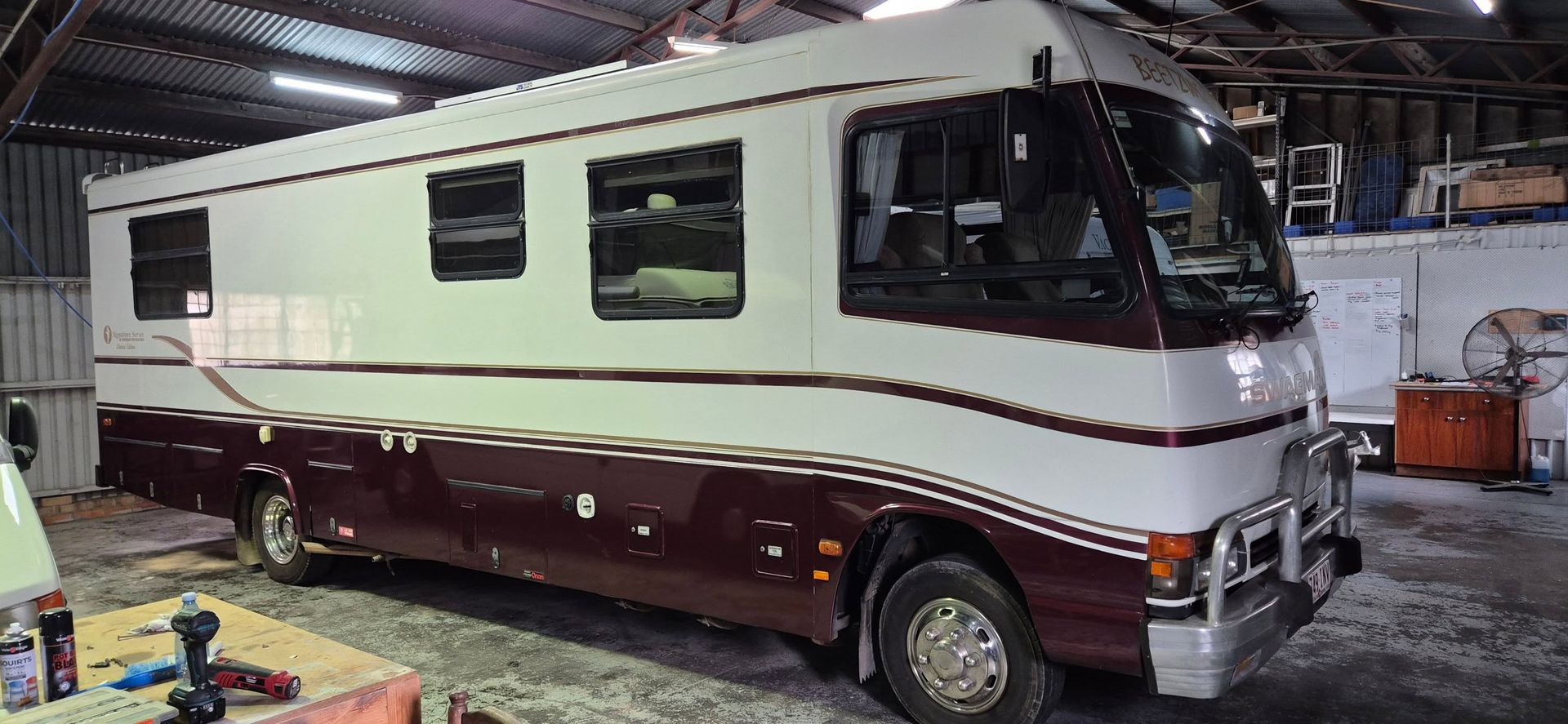 White camper trailer with extended awning and ramp on a sunny campsite.