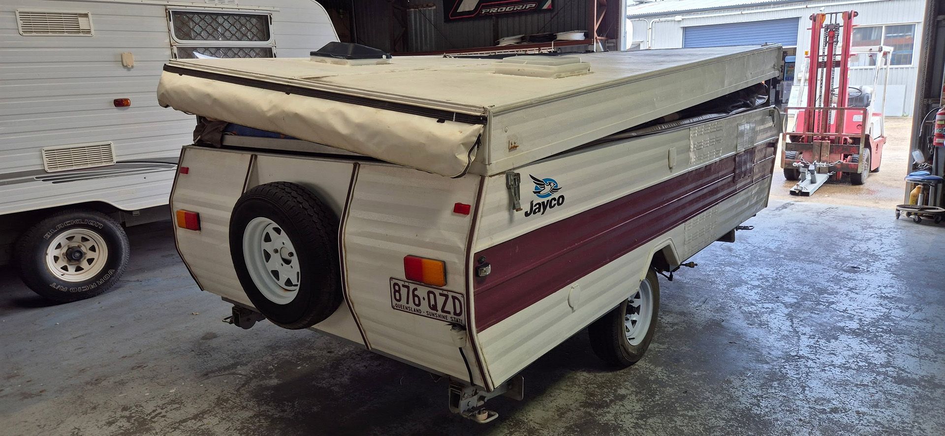 A white campervan with an extended awning. Two ladders stand near the van, inside a garage — Revive Caravan Repairs in Kippa-Ring, QLD