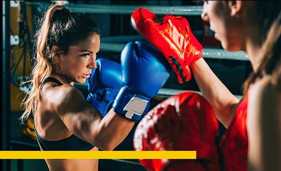Two women boxing in a ring; one with blue gloves, the other with red, both throwing punches.