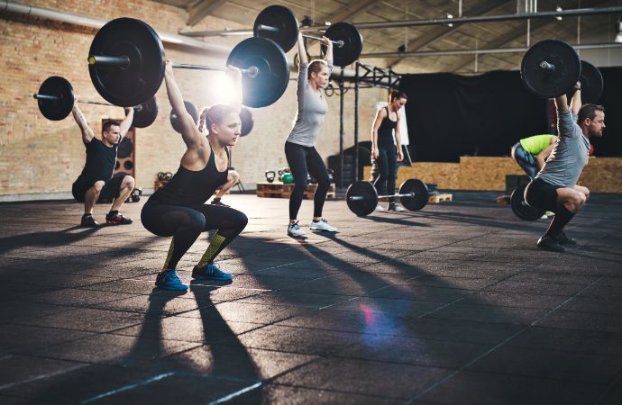 People lifting barbells overhead in a gym, squatting.