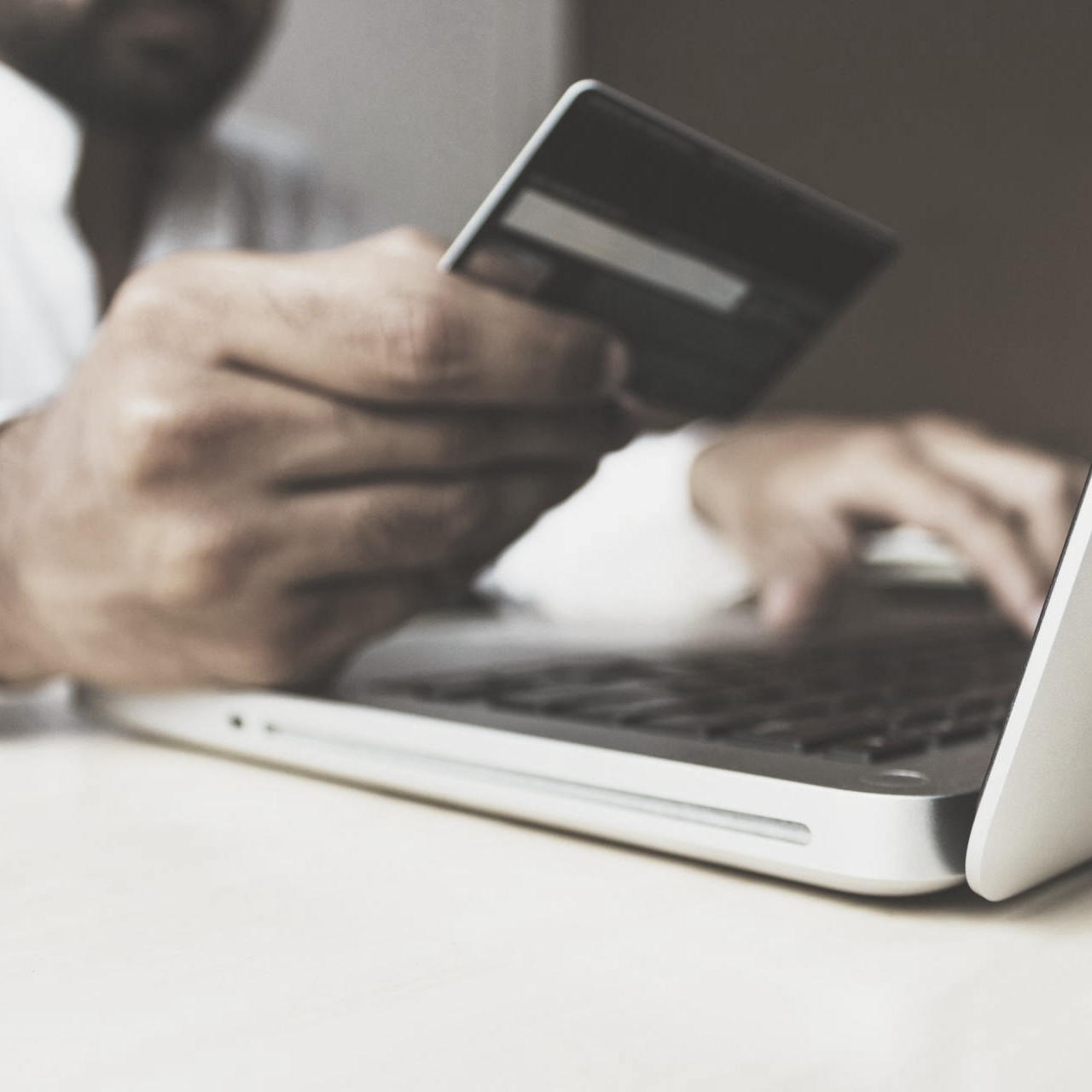 Person holding a credit card over a laptop, likely for an online purchase.