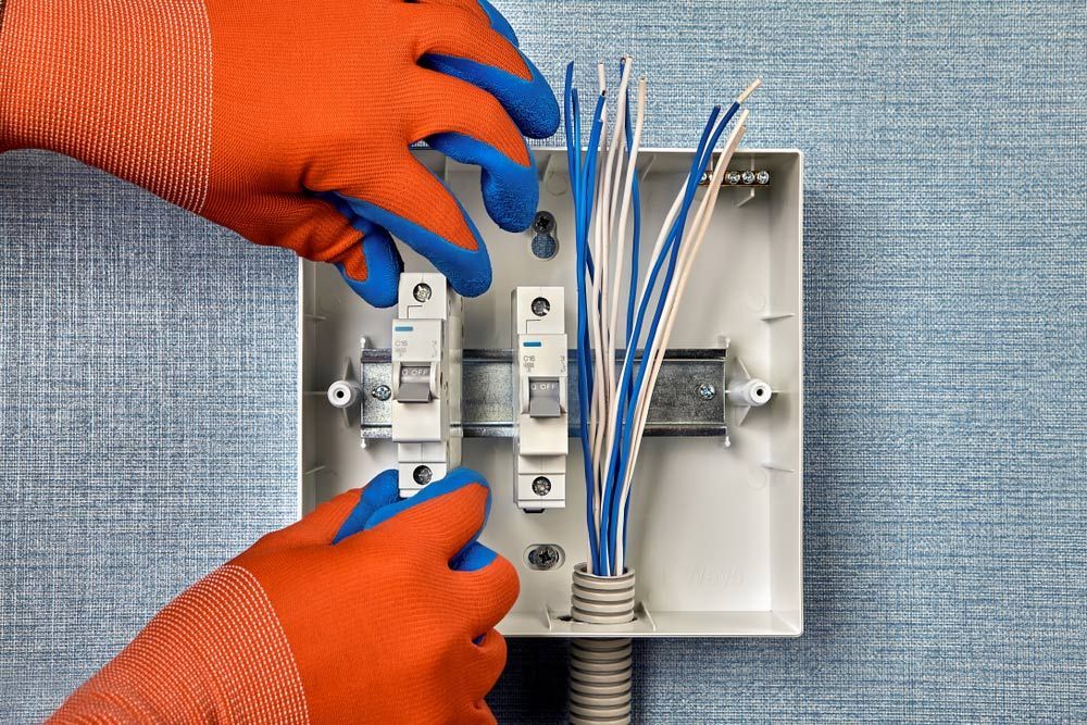 A Person Wearing Orange And Blue Gloves Is Working On An Electrical Box — Switchboard Upgrades In Wagga Wagga, NSW