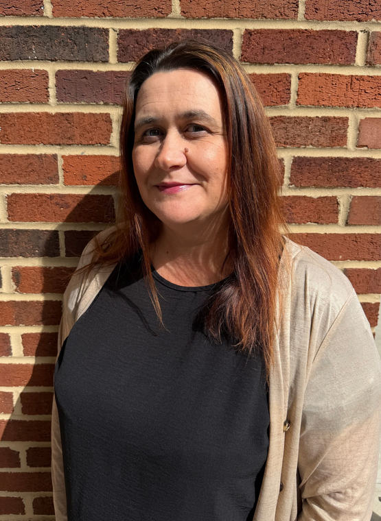 A woman with long red hair is smiling in front of a brick wall.