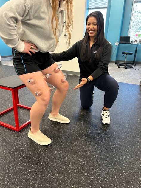 A woman is kneeling down next to a woman with pins on her legs.