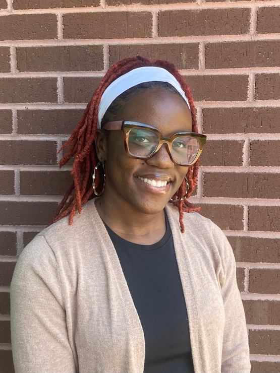 A woman in a black scrub top is smiling in front of a brick wall.