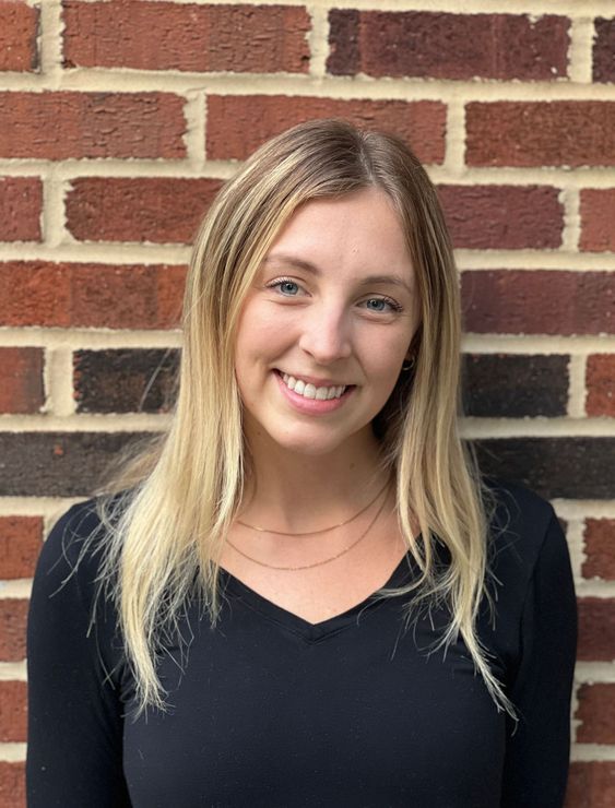 A woman in a black shirt is smiling in front of a brick wall.