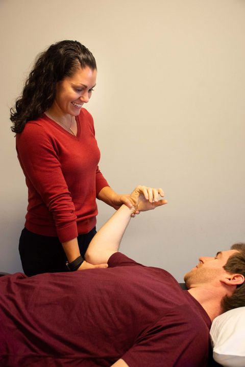 A woman in a red sweater is stretching a man 's arm