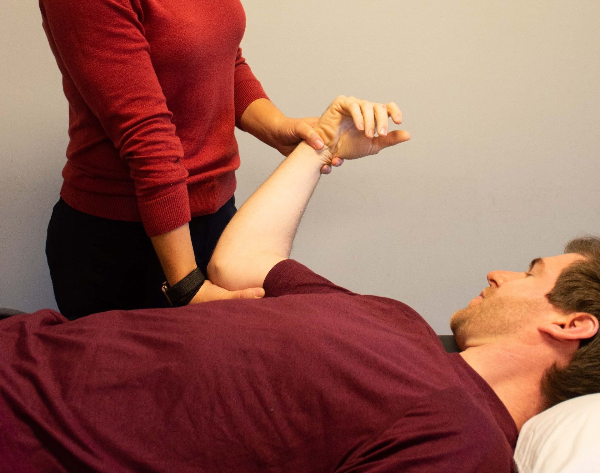 A woman in a red sweater is stretching a man 's arm