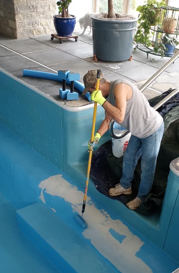 A man is painting a swimming pool with a brush.